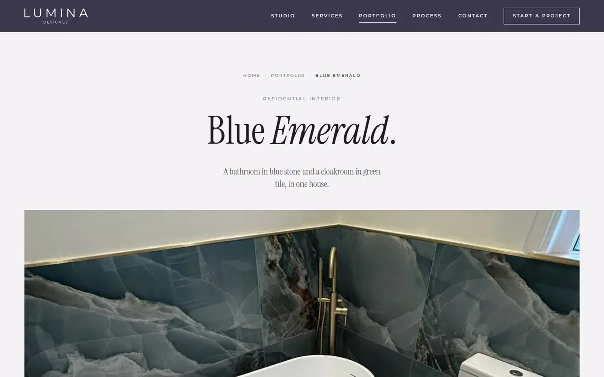 A project page on a design and build company website, with a breadcrumb trail, the project name in large serif type and a photograph of a finished bathroom in blue stone tiles